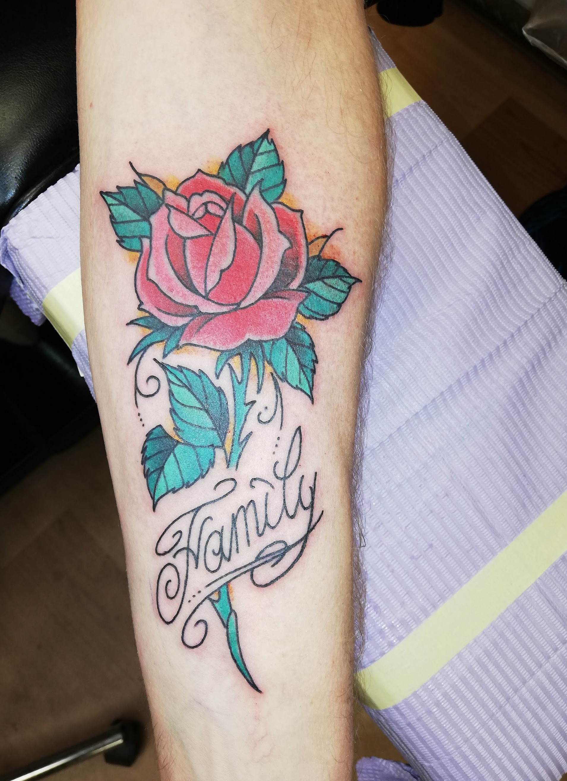 Roze roos met een banner waarin Family staat, op een onderarm